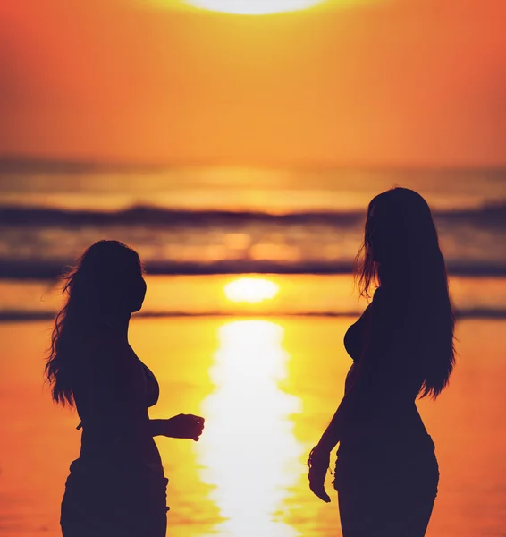 Silhouettes of two girls against red sunset on the beach