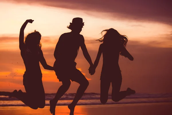 Silhouettes of happy young friends jumping on the beach  against red sunset