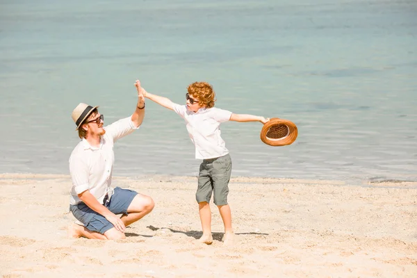 Hipster father with beard and red haired son playing on the beach at a sunny day. Concept of friendly family