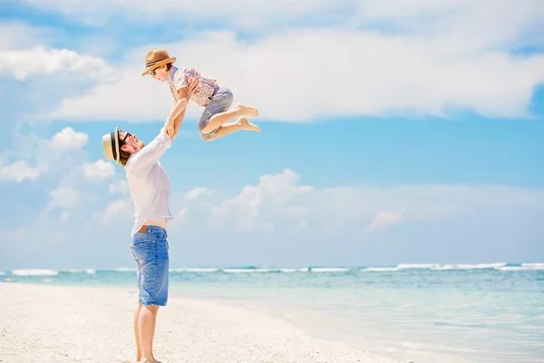 Young happy father playing with his little son standing barefoot at the beach against ocean and beautiful clouds on background