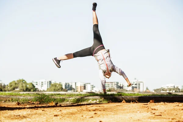 Young fit woman doing simple acrobatics exercise routine in autumn park with city at background