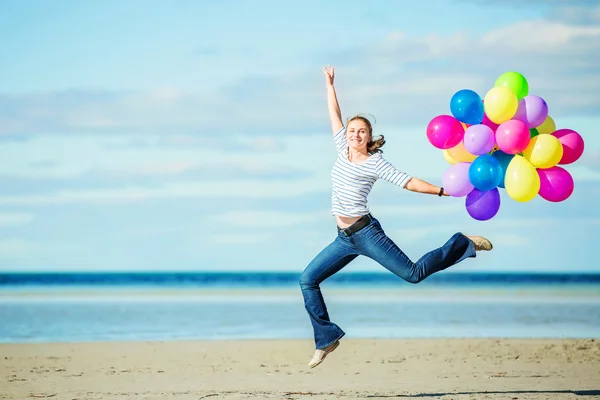 Beautiful girl jumps on the beach while holding colored balloons