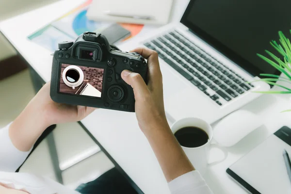 Photographer holding camera checking photo on her desk workspace