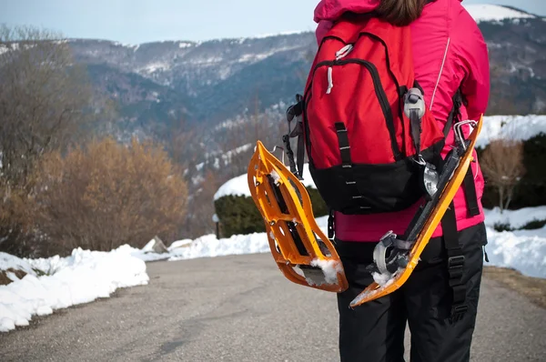 Woman on the road with snowshoes  hung in the back