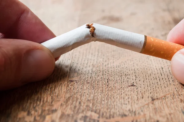 Stop cigarette concept - closeup of man broken a cigarette  on wooden table background