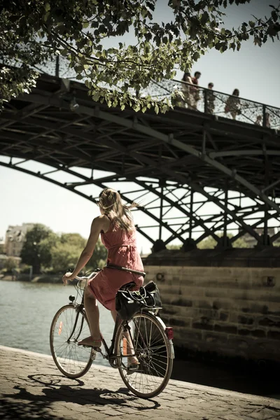 PARIS - France - 23 July 2012 - blond woman with bike under the bridge of arts in Paris