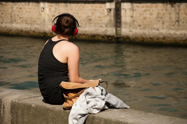 Woman listening music with red Headphone in border Seine river in Paris