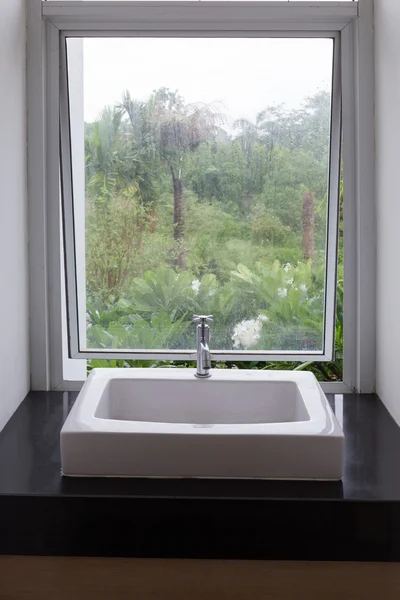 Washbasin in bathroom with transparent mirror window nature view