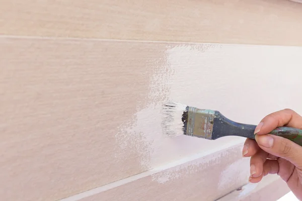 Hand worker holding brush painting white on wood fence