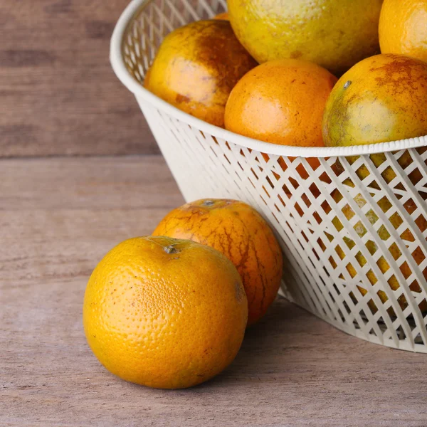 Orange fruit in white basket on wood table background