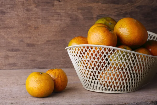 Orange fruit in white basket on wood table background
