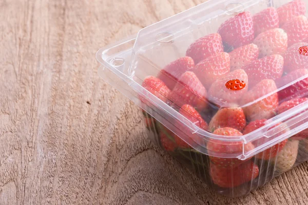 Red ripe strawberry in plastic box of packaging on wood table