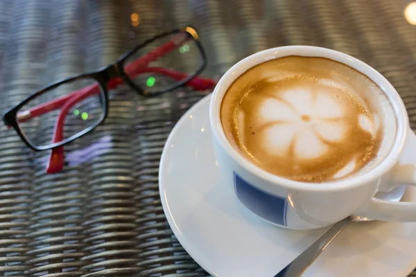 Hot latte coffee, white coffee cup on table with eyeglasses