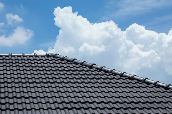 Black tile roof of house with blue sky and cloud background