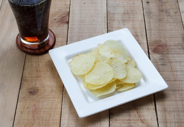 Potato chips and soft drink in glass on wood background, Selecti