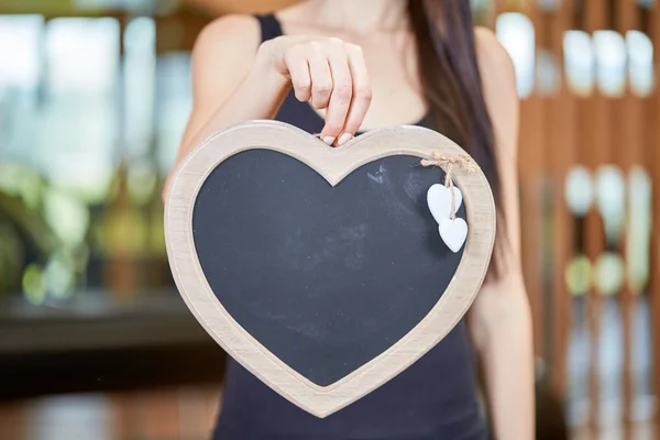 Young caucasian woman holding blackboard in form of heart