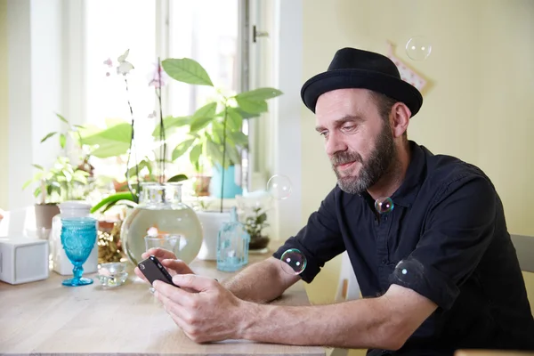 Man with hat and beard happy looking at phone and soap bubbles i
