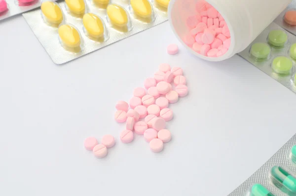 Packaging medicine tablet around open bottle of pink medicine table