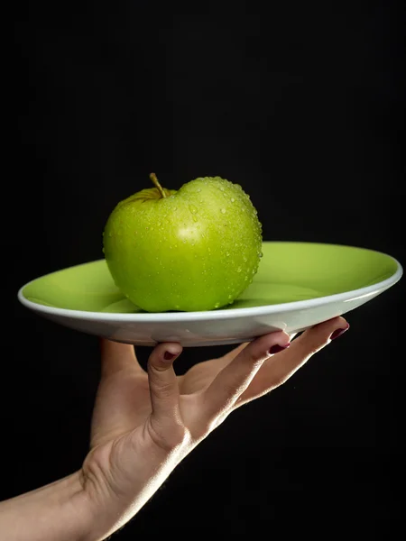 Green apple on plate in hand