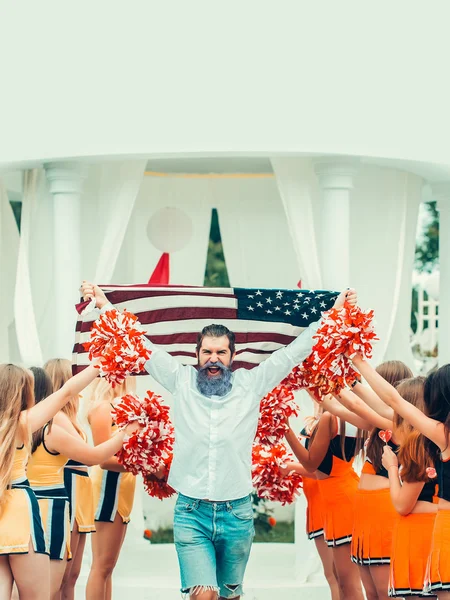 Man with american flag and cheerleader team