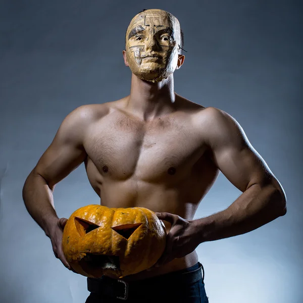 Muscular man in mask with pumpkin