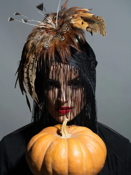 Pretty sexy woman in feather hat holds pumpkin