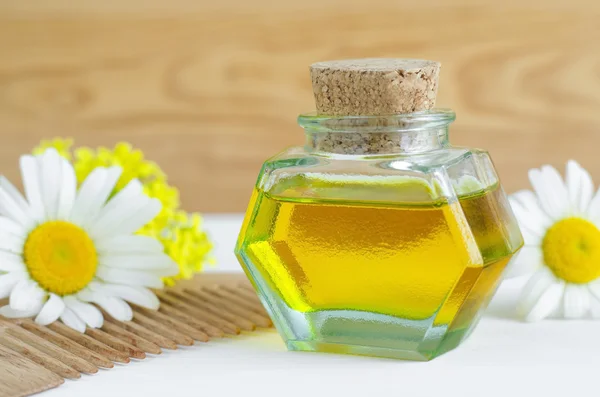 Small bottle of cosmetic chamomile oil and wooden hair comb