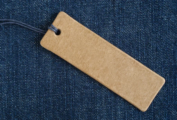 Blank paper label on a blue denim fabric. Jeans background with sale or price tag.