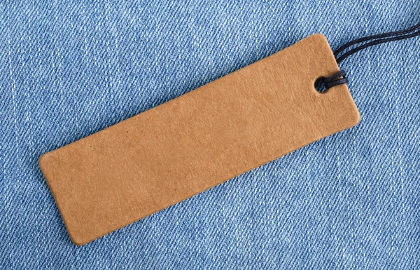 Blank paper label on a light blue denim fabric. Jeans background with sale or price tag.