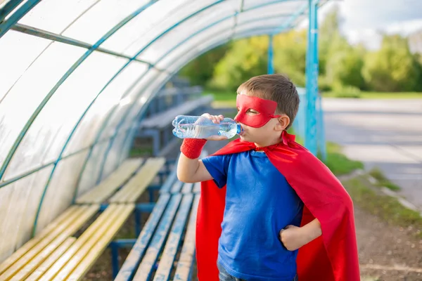 Superhero standing under canopy and drinking water from a bottle