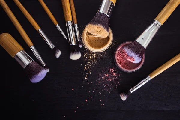 Make up brushes with powder and rouge on a black wooden background