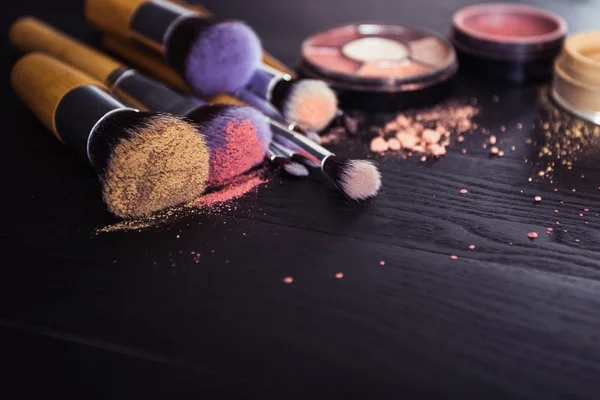 Make up brushes with powder and rouge on a black wooden background