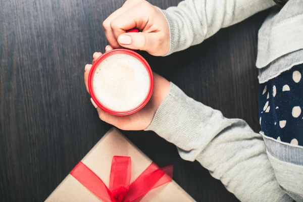 Woman holding a red cup of coffee. gift box with red ribbon.
