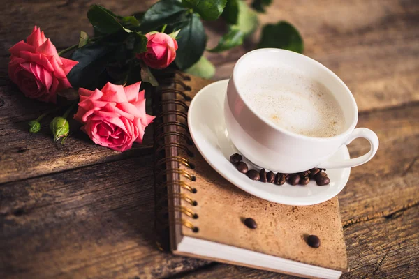 Cup of coffee with milk and pink roses and books on the old wooden background