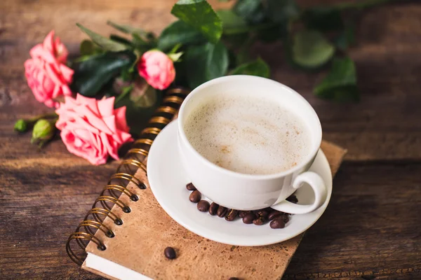 Cup of coffee with milk and pink roses and books on the old wooden background