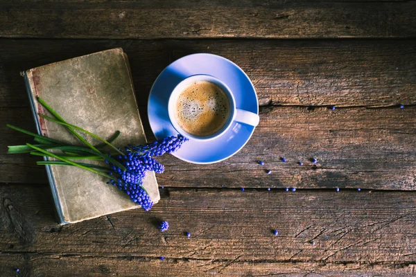 Blue flowers and a cup of coffee with a book on a wooden background
