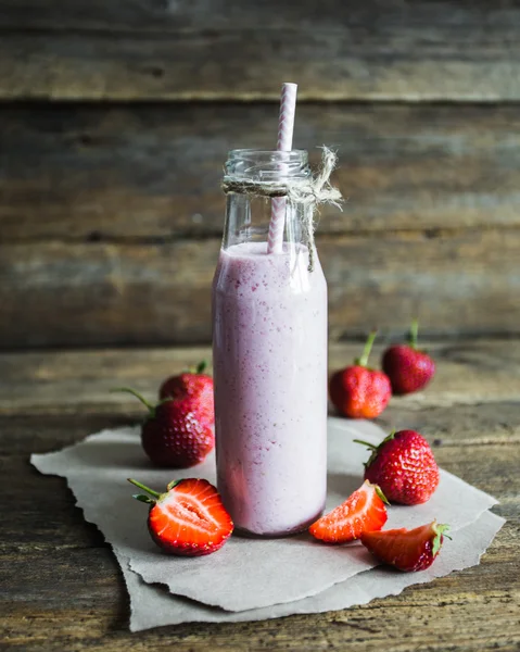 Glass of strawberry smoothie and fresh strawberries on a wooden background