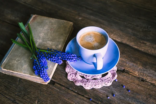 Blue flowers and a cup of coffee with a book on a wooden background