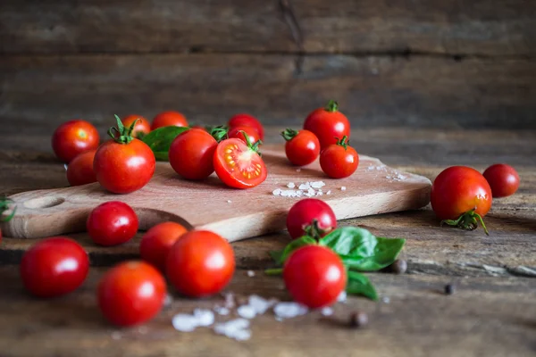 Fresh grape tomatoes with basil and coarse salt for use as cooking ingredients on kitchen board