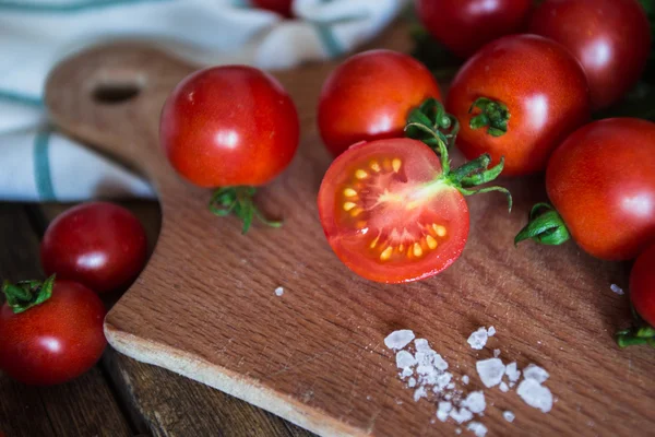 Fresh grape tomatoes with basil and coarse salt for use as cooking ingredients on kitchen board