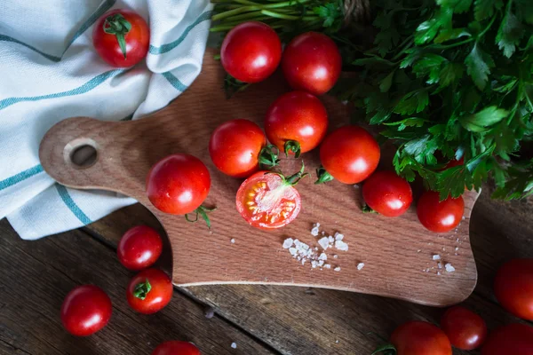 Fresh grape tomatoes with basil and coarse salt for use as cooking ingredients on kitchen board