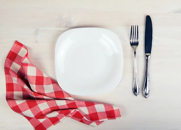 Empty dish, knife and fork and red napkin on wood table