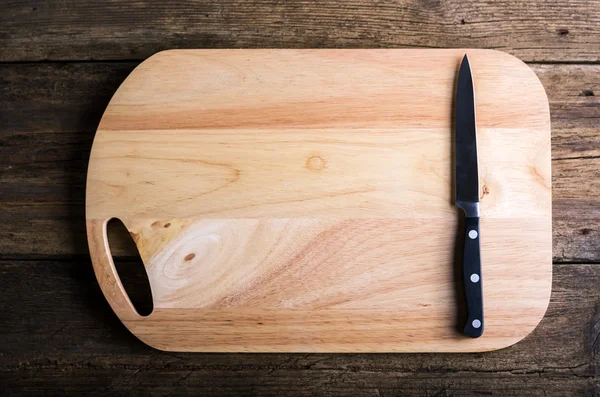 Empty chopping board with a sharp paring knife on a distressed grunge wooden table in a rustic kitchen, overhead view with a vignette and copyspace