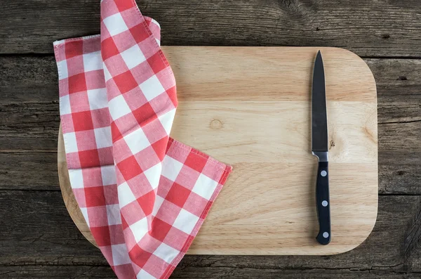 Empty chopping board with a sharp paring knife and napkin on a distressed grunge wooden table