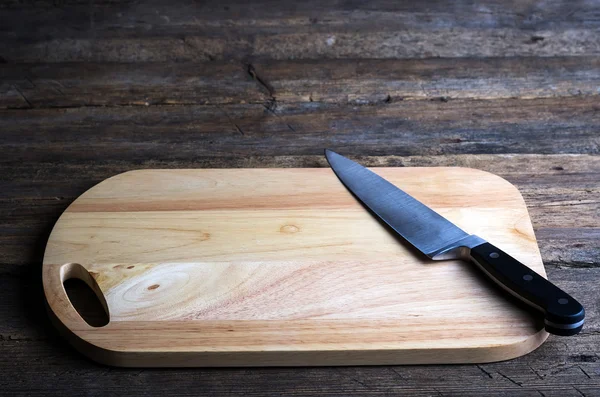 Empty chopping board with a sharp paring knife on a distressed grunge wooden table in a rustic kitchen, overhead view with a vignette and copyspace