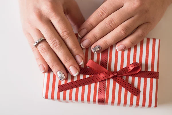 Beautiful gel lacquer. French manicure with silver diamonds. red gift box with a white bow in the hands of a girl