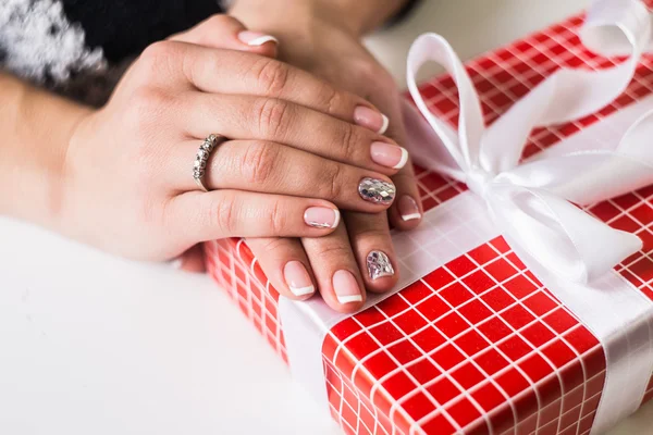 Beautiful gel lacquer. French manicure with silver diamonds. red gift box with a white bow in the hands of a girl
