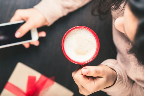 Woman holding a smart phone and a red cup of coffee. gift box wi