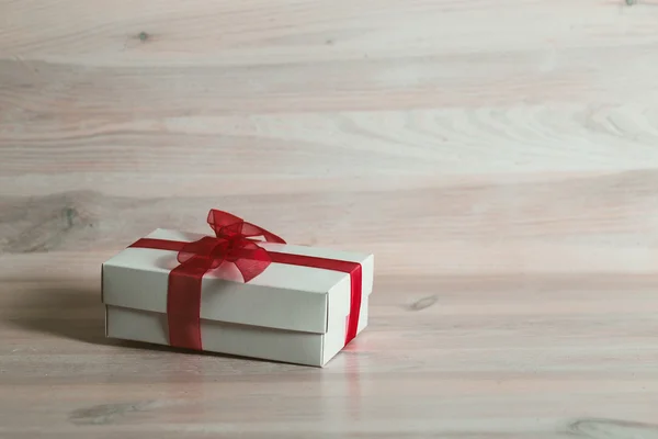 Gift box with red ribbon on a white wooden table.