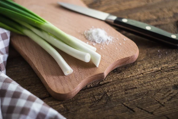 Green onions on a chopping board. Knife and napkin on a wooden table